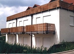 Weiße Hausfassade mit Stahlbalkonen und Holzgeländern